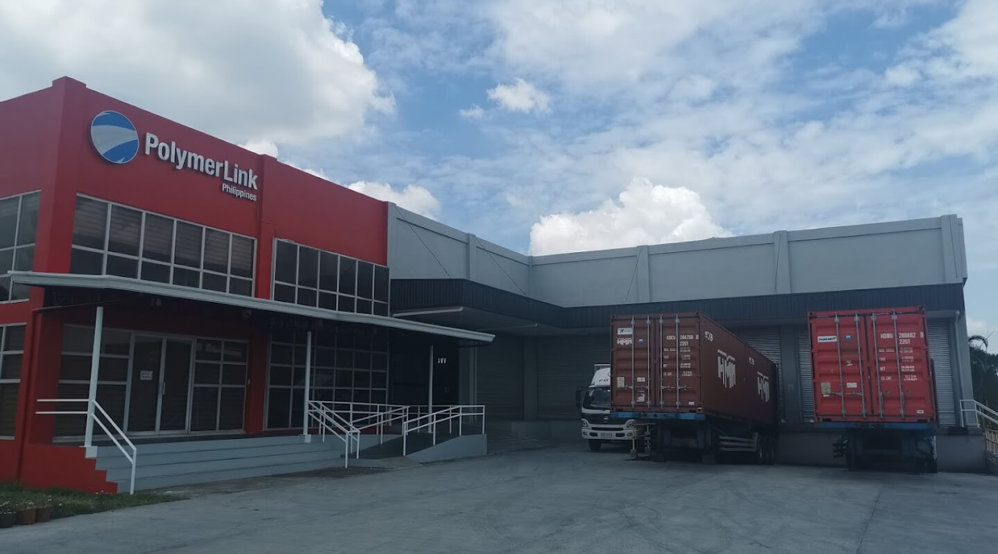 Polymer Link (Phils.) Inc. located in the Philippines, is the red and white coloured building with three lorries parked in front of it