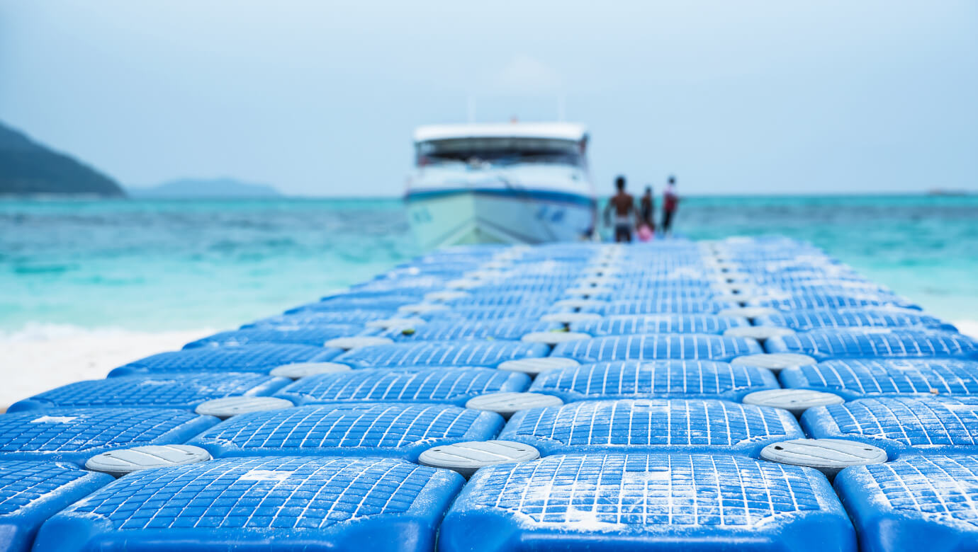 Blue floating docks are made using Masterbatch Solutions by Polymer Link, located near the sea with a ship docked