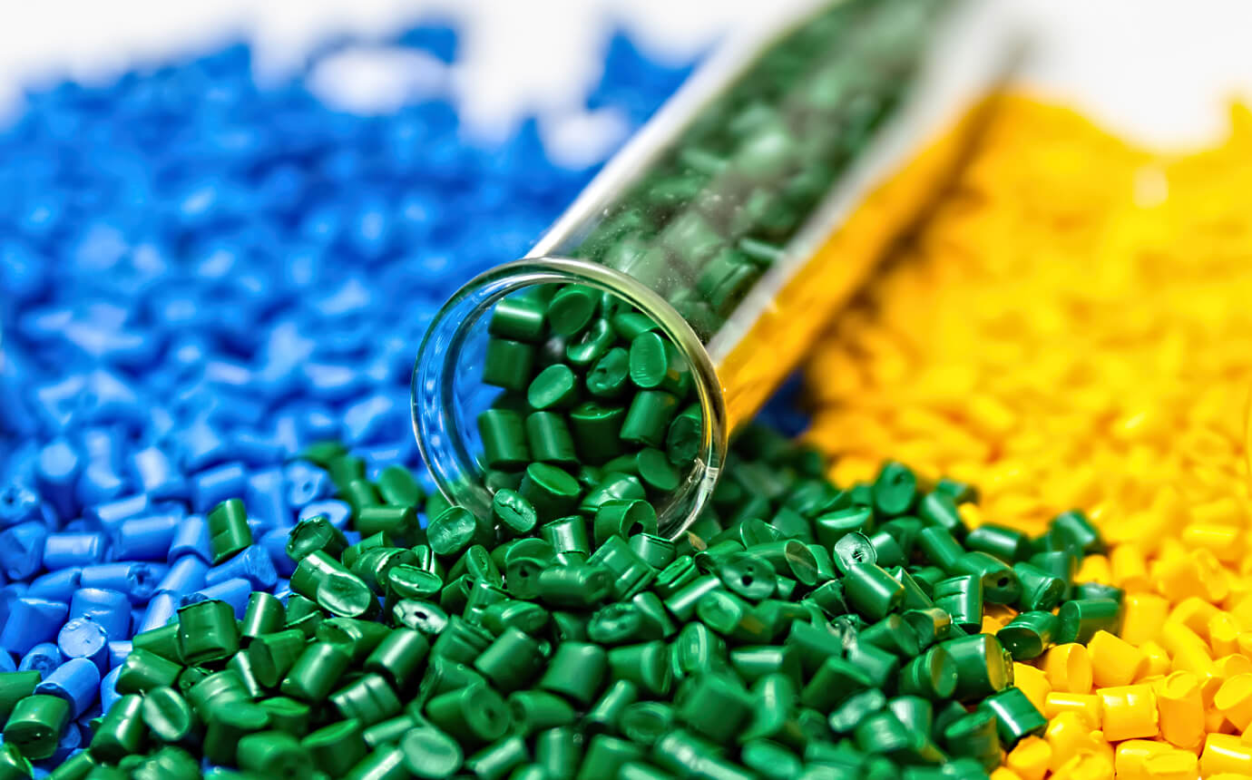 Green coloured masterbatches are overflowing from a tube lying down, while blue and yellow coloured masterbatches in the background, are all manufactured by Polymer Link