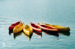 Red and yellow Polymer Link kayaks grouped together on a tranquil and reflective blue water surface, embodying leisure and the high-quality craftsmanship of Polymer Link products