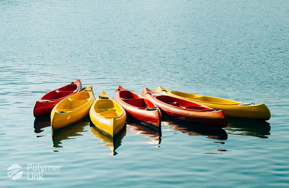 Red and yellow Polymer Link kayaks grouped together on a tranquil and reflective blue water surface, embodying leisure and the high-quality craftsmanship of Polymer Link products