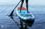 Stand-up paddleboarder balancing on a Polymer Link paddleboard, showcasing the stability and design of water sports equipment on a serene lake